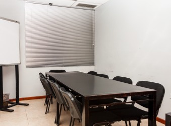 Salón con mesa de reuniones, sillas, persianas y una pizarra blanca