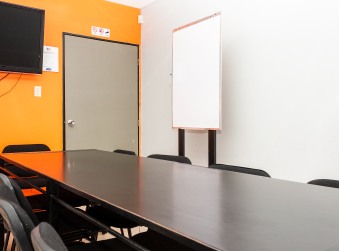 Salón con mesa de reuniones, un televisor en una pared naranja y una pizarra blanca
