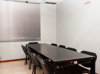 Salón con mesa de reuniones y sillas frente a una ventana con persianas