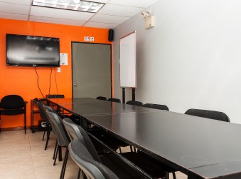 Salón con una mesa larga de reuniones, sillas y un televisor en una pared naranja