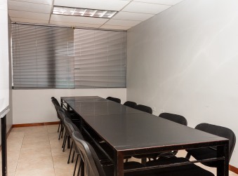 Salón con una mesa larga de reuniones y sillas junto a una ventana con persianas